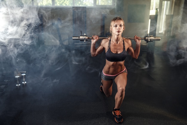 Young sexy girl in the gym doing squat on smoke background