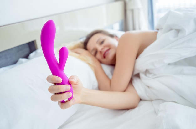 Young sexy woman in the bed holding in her hands a sex toy for adults