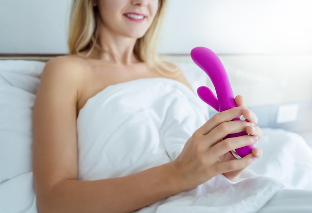 Young sexy woman in the bed holding in her hands a sex toy for adults