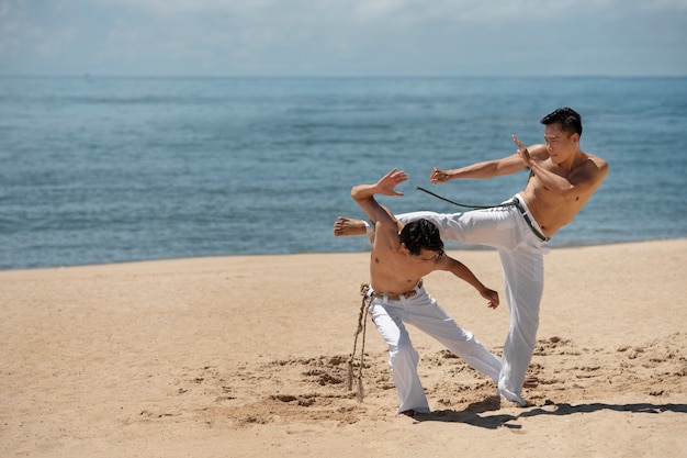 Young shirtless men practicing capoeira together on the beach