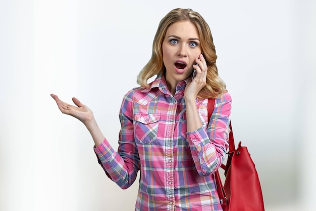 Young shocked woman talking on cell phone on blurred background. People, modern technology, communication and emotions concept.