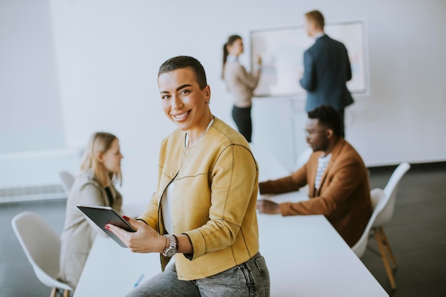 Young short hair business woman standing in the office and using digital tablet in front of her team