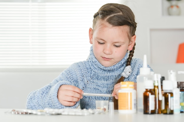 Young sick girl with thermometer sitting at table