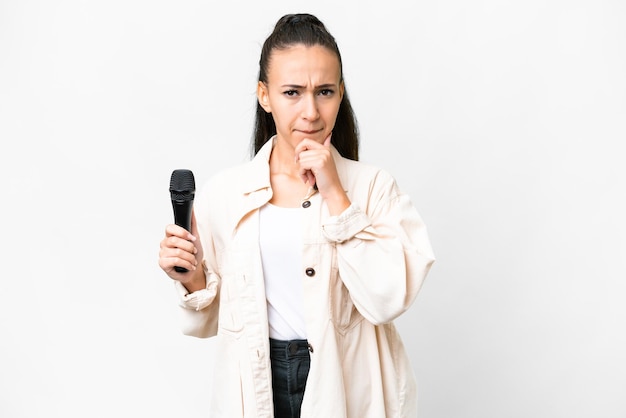 Young singer woman picking up a microphone over isolated white background having doubts and thinking