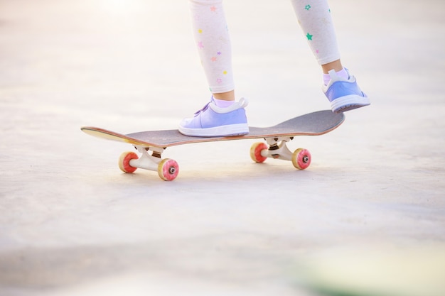 young skateboarder girl legs riding on skateboard on green grass