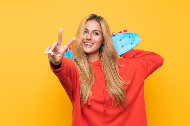 Young skater woman making victory gesture over isolated yellow