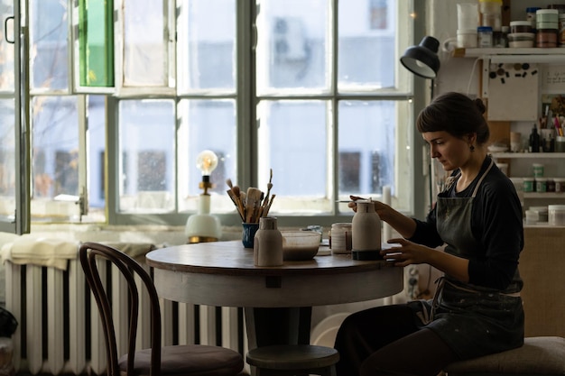 Young skilled lady concentrated on modeling jug from raw clay enjoys hobby creating vase