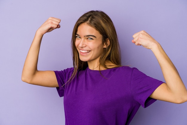 Young skinny caucasian girl teenager on purple background showing strength gesture with arms, symbol of feminine power