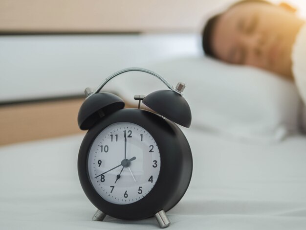 Young sleeping man and alarm clock in bedroom at home