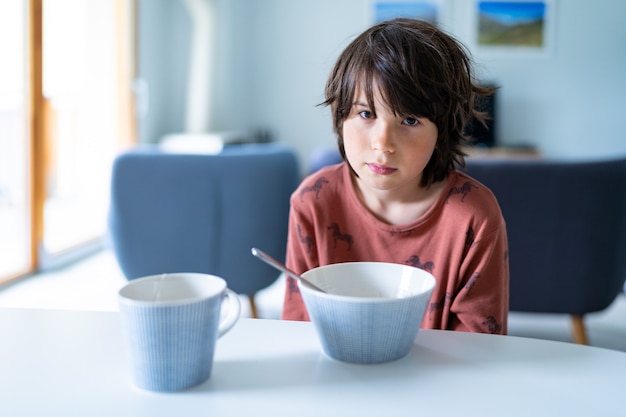 A young sleepy boy wearing pajamas taking breakfast at home in the morning before school. Healthy food for children.