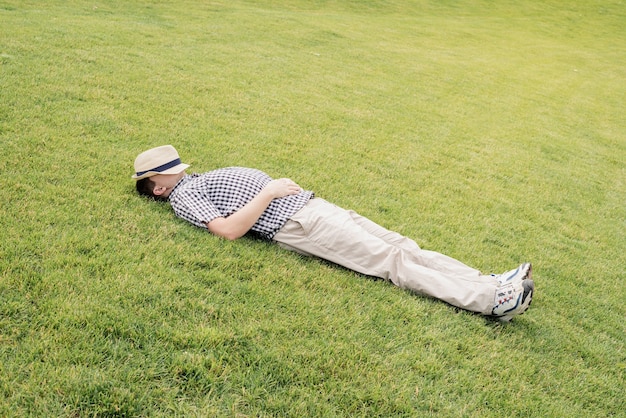 Photo young sleepy man with a hat over his face laying down in the grass