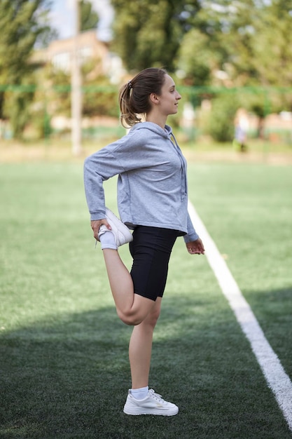 A young slender beautiful woman warms up warms up her muscles in the summer on an artificial turf