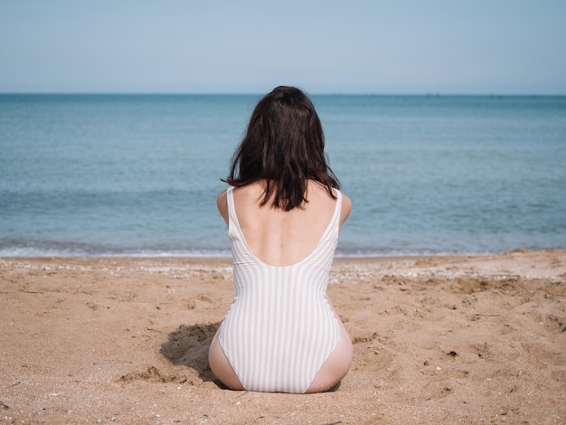 A young slender girl in a bikini is relaxing on a sandy beach on an island Summer lifestyle background The concept of travel tourism Relaxing by the sea solitude meditation relaxation