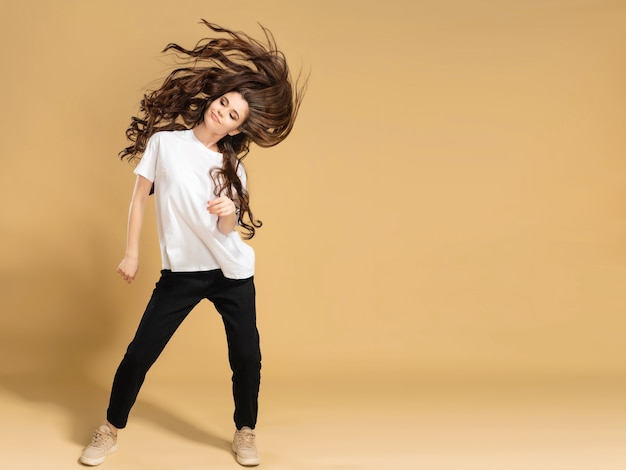 Young slender girl in a white t-shirt dancing and waving long hair on a pastel orange.