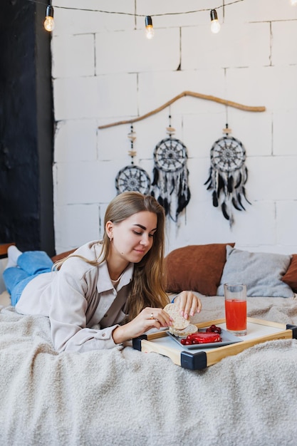 A young slender woman is sitting on the bed and eating a delicious breakfast of rice cakes and fresh juice Healthy Eating