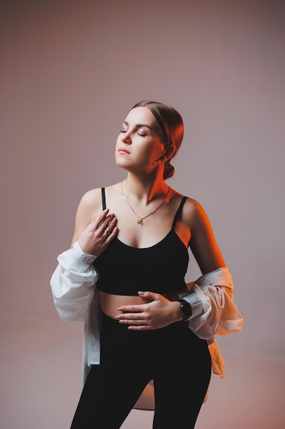 A young slender woman in a white shirt and black pants with makeup on her face poses on a plain background Stylish European woman in a black top