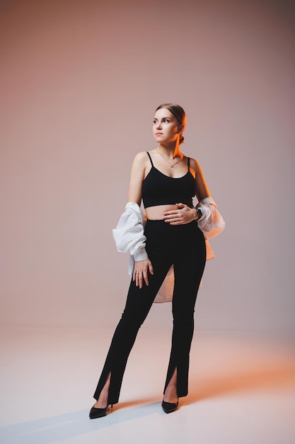 A young slender woman in a white shirt and black pants with makeup on her face poses on a plain background Stylish European woman in a black top