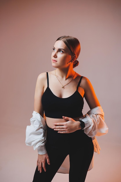 A young slender woman in a white shirt and black pants with makeup on her face poses on a plain background Stylish European woman in a black top