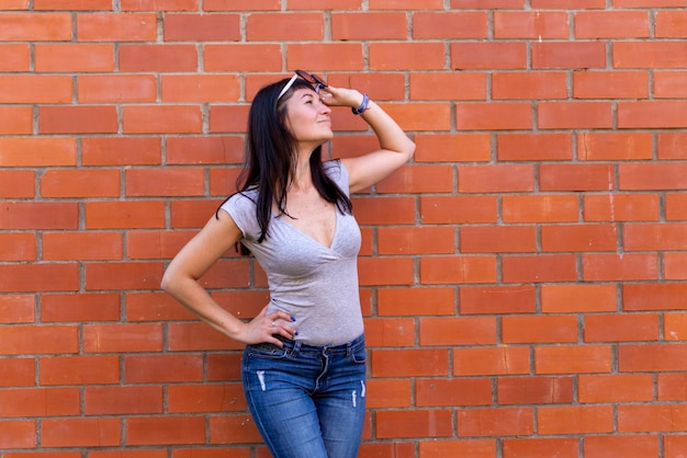 Young slender woman with glasses looking up against a brick wall background