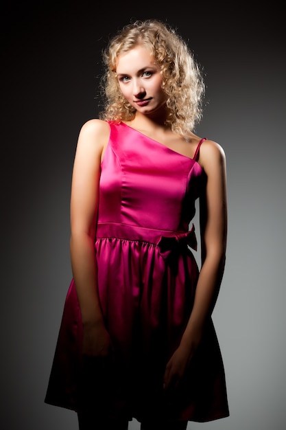 Young slim beautiful blond woman with curly hair in purple dress standing