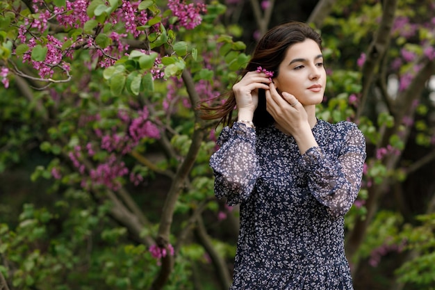 Young slim female wearing stylish dress standing looking aside putting blossom in hair