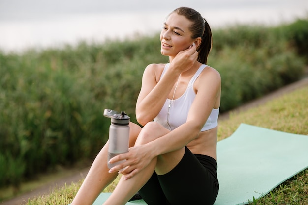 Young slim fit woman with earphones and smartphone listen music in the park at the sunny day