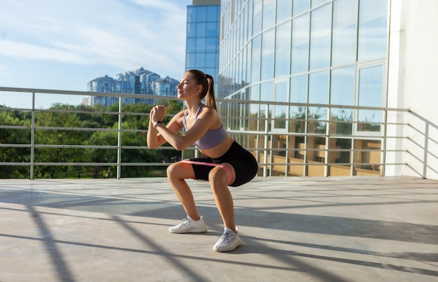 Young slim fit woman working out with fitness rubber bands outdoors in the city