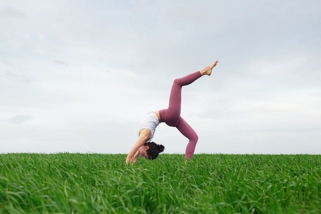 Young slim girl doing yoga outdoors in a green field