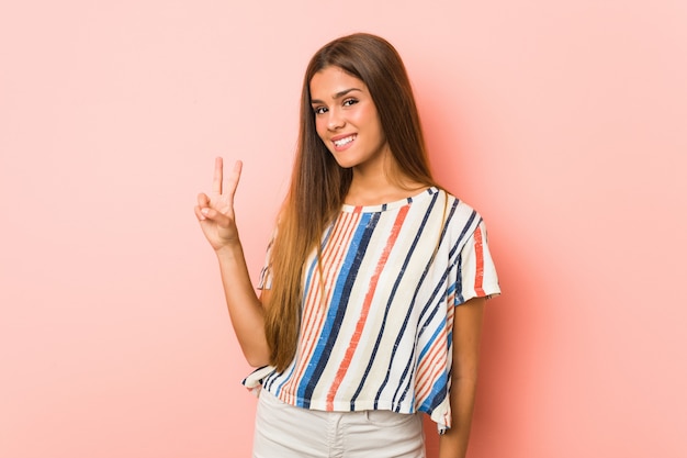 Young slim woman showing victory sign and smiling broadly.