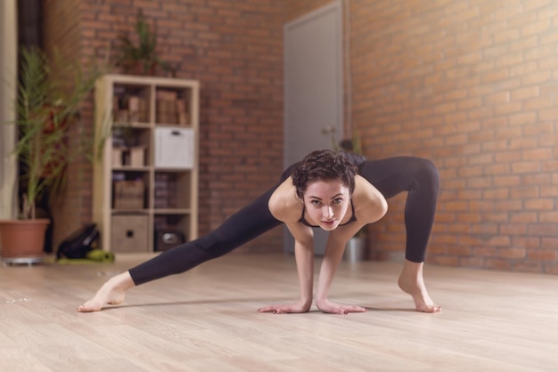 Young slim woman standing on tiptoe doing stretching exercise bending forward facedown indoors in fitness club