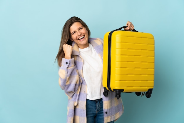 Young Slovak woman isolated on blue wall in vacation with travel suitcase