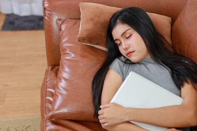 Young smart and active asian female lying and sleeping on sofa in living room with tablet, Lifestyle and technology.