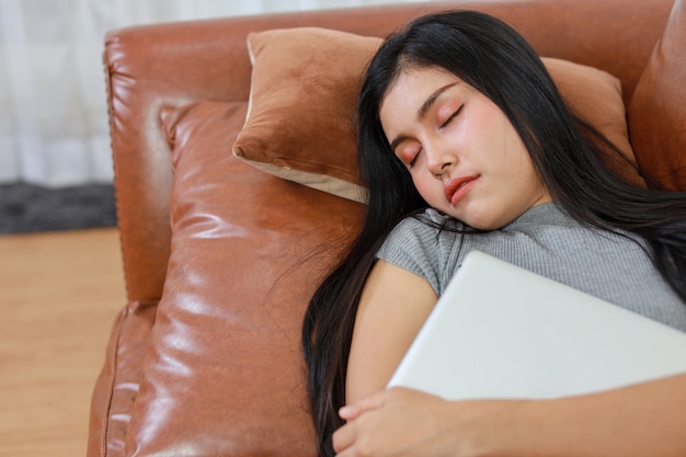 Young smart and active asian female lying and sleeping on sofa in living room with tablet, Lifestyle and technology.