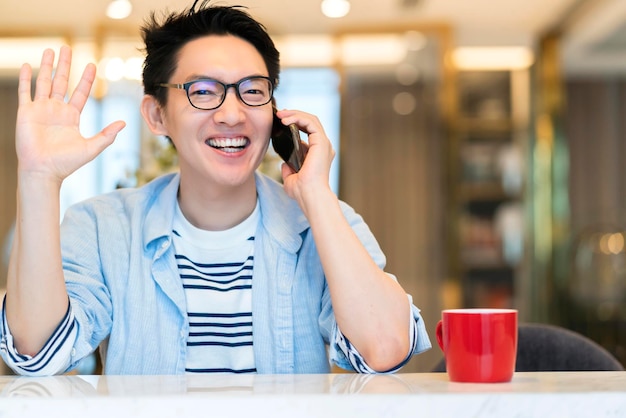 Young smart asian female wear glasses casual shirt say hi and hand communication with smartphone technology white toothly smile and welcome cheerful room interior background