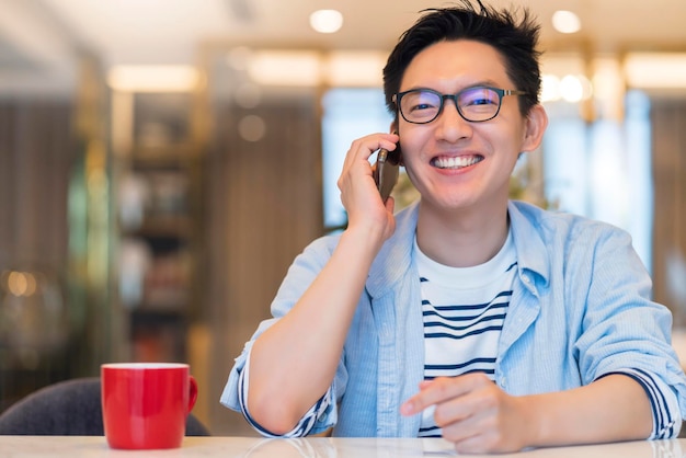 Young smart asian male wear glasses casual shirt say hi and hand communication with smartphone technology white toothly smile and welcome cheerful room interior background