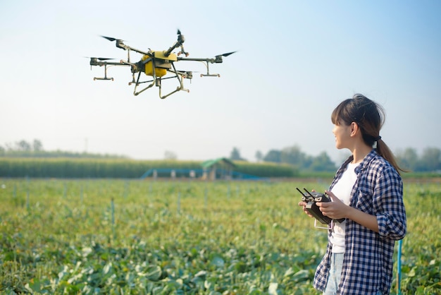 A young smart farmer controlling drone spraying fertilizer and pesticide over farmland