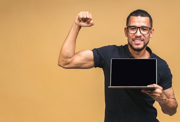 Young smiling african american black man standing and using laptop computer isolated over beige background Showing pc screen