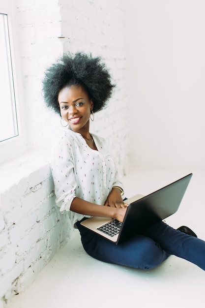 Young smiling african american business woman using the laptop, sitting on the floor