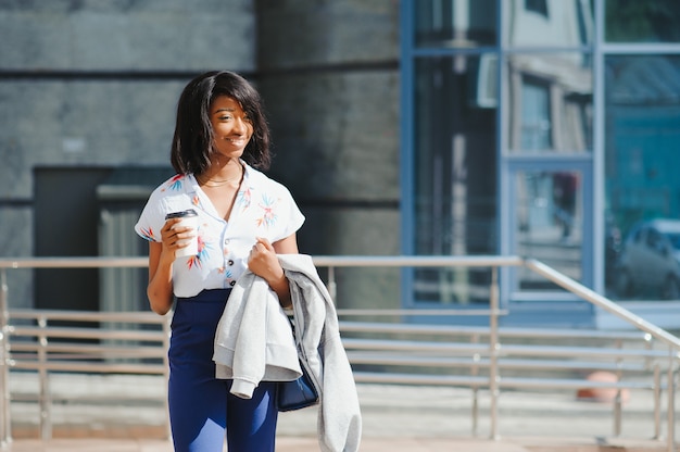 young smiling african american businesswoman with coffee cup in city