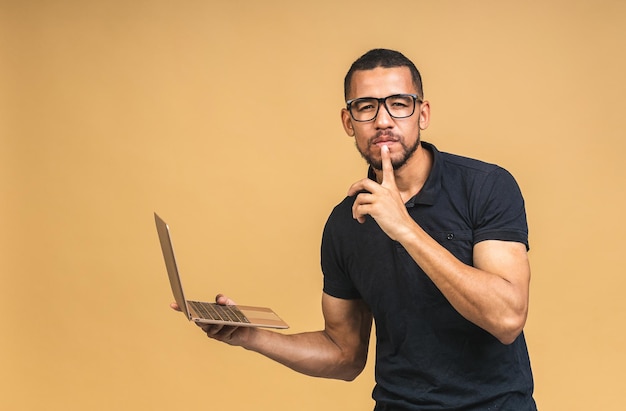 Young smiling african american man standing and using laptop computer isolated over beige background