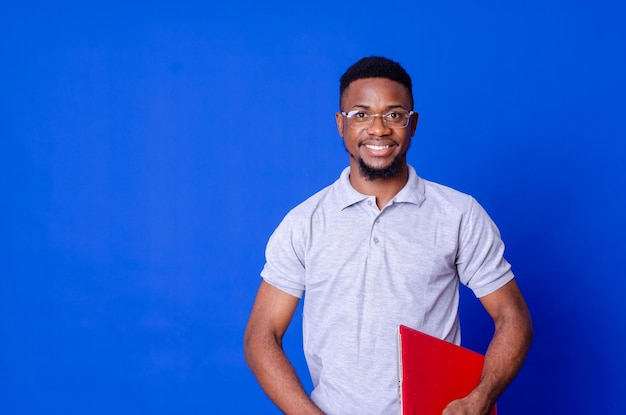 Young smiling african american man standing and using laptop computer isolated over blue background