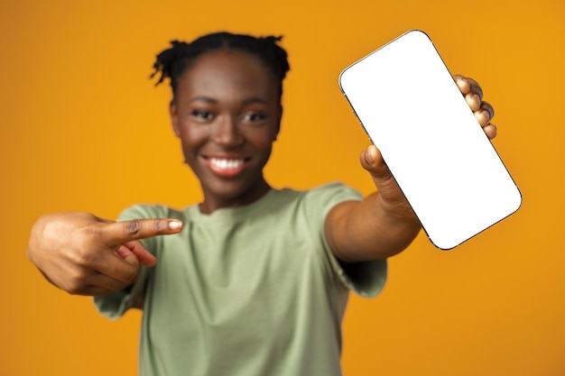 Young smiling african american woman showing smartphone with blank screen against yellow background