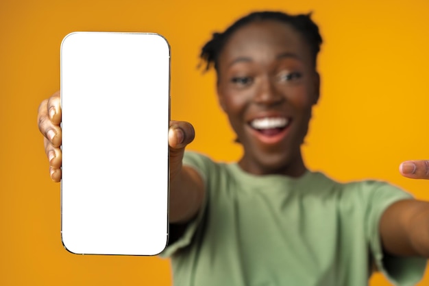 Young smiling african american woman showing smartphone with blank screen against yellow background