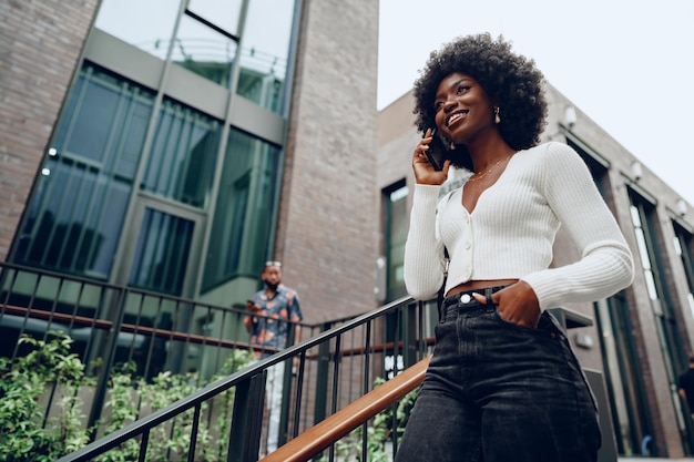 Young smiling african woman using smartphone going downstairs in the city