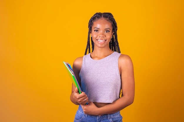 Young smiling afro girl happy teenage student holding books and notebooks on background with free space for text