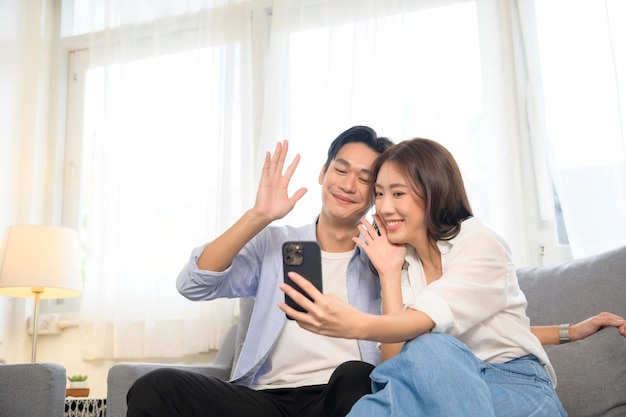 Young smiling asian couple holding smartphone and making video call at home