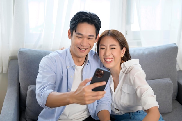 Young smiling asian couple using smartphone in living room at home