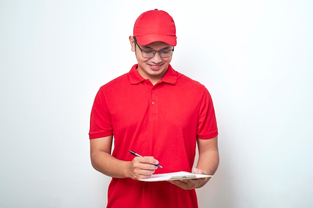 Young smiling asian delivery man in red uniform and cap holding clip board