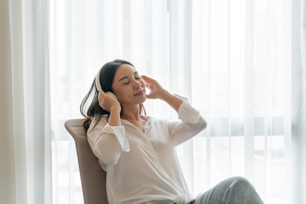 Young smiling Asian woman sitting and listening music Young brunette girl relaxing at home in a leisure timex9Copy space