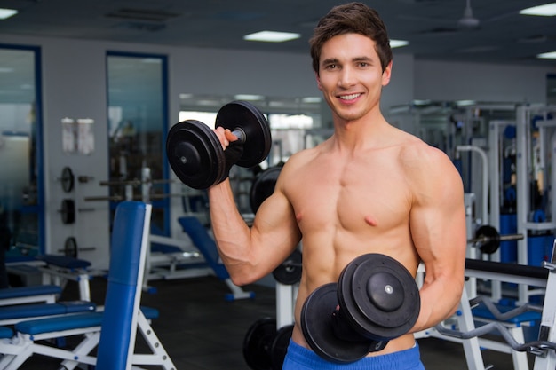 Young smiling athlete lifting weights in the gym and smail